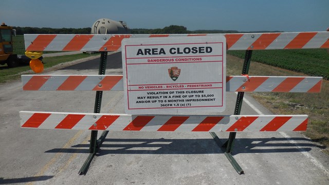 An orange and white wooden barrier with a sign stating road closed. 